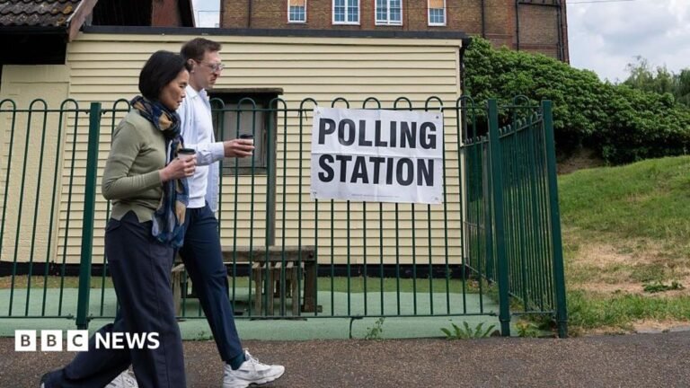 Local election candidates told to respect each other as abuse rises Two people walk past a polling station sign on a green fence.