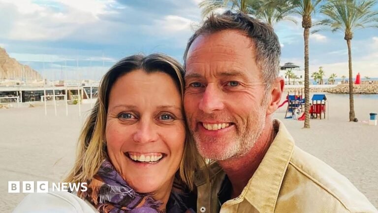 No regular contact with couple held in Iran, family say A couple on a beach. It is sunny and the sand is white. Behind them are some trees.