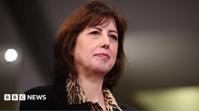 Close-up of Lucy Powell as she looks off to the right. She is wearing a leopard print blouse and black suit jacket