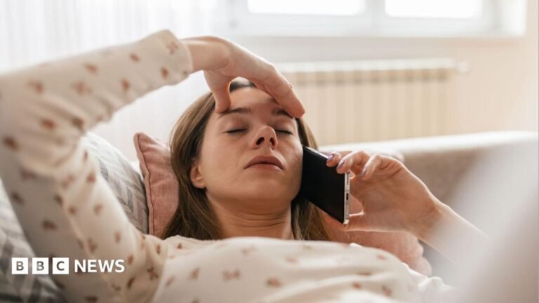 Off sick? You need to phone your boss, back-to-work adviser says Woman lying back on a sofa with one hand on her forehead and the other hand holding a mobile phone to her ear