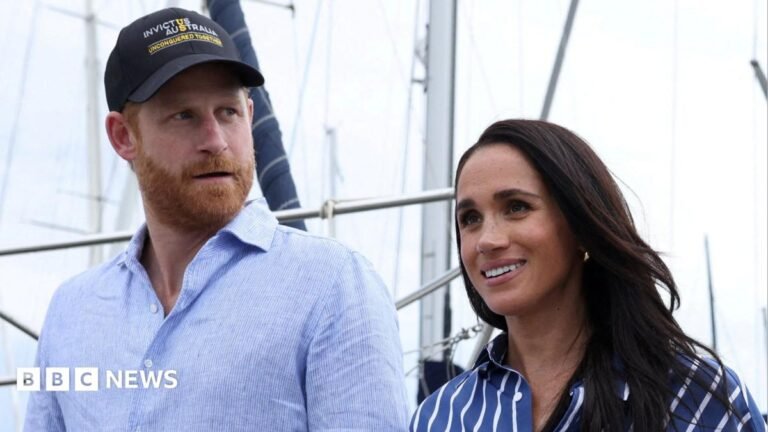 Prince Harry and Meghan not working royals, says King A woman with short reddish hair with a neutral expression faces the camera while sitting a room with black and brown wallpaper.