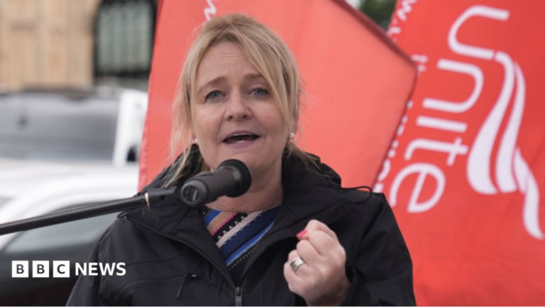 Scrapping pensions triple lock ‘morally wrong’, says union boss Head and shoulders shot of Graham, who has blonde hair pulled back in a ponytail and is wearing a black raincoat over a striped blue and black top. She has her fist clenched with red nail varnish visible and two wedding rings. She is standing in front of a red Unite the Union flag.