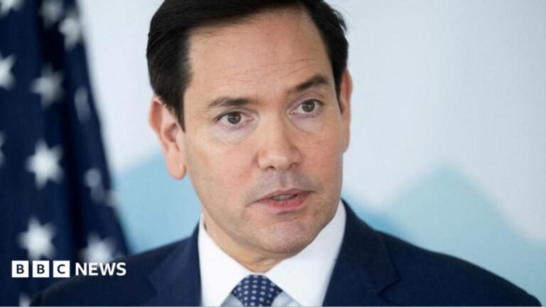 A close-up of Marco Rubio wearing a dark suit with white shirt and dotted tie