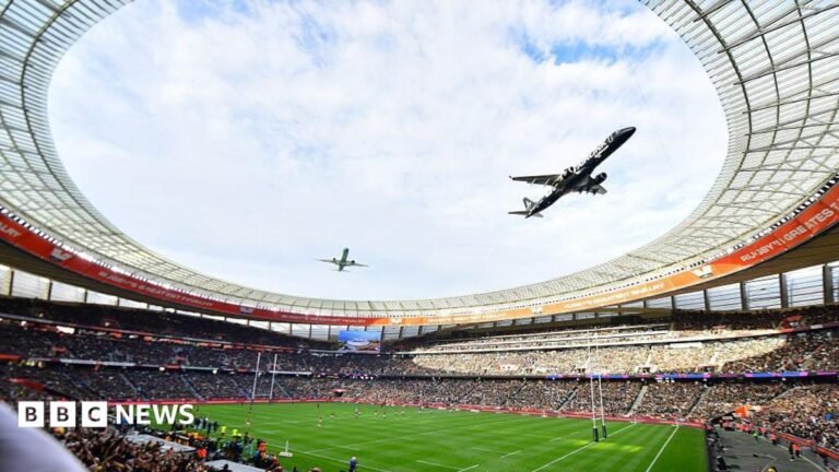 A fish-eye view from the stands of a rugby stadium looking up at the sky as two planes fly in close formation above.