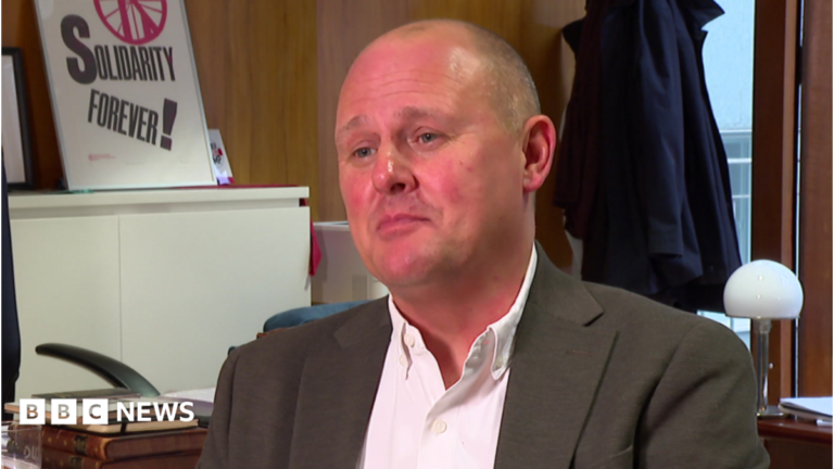 Tax banks to give some households energy bill cut, unions tell PM TUC general secretary Paul Nowak sitting in his office. He is pictured in a grey suit and white shirt, worn without a tie. Behind him is a desk and a poster with the phrase Solidarity Forever! on it.