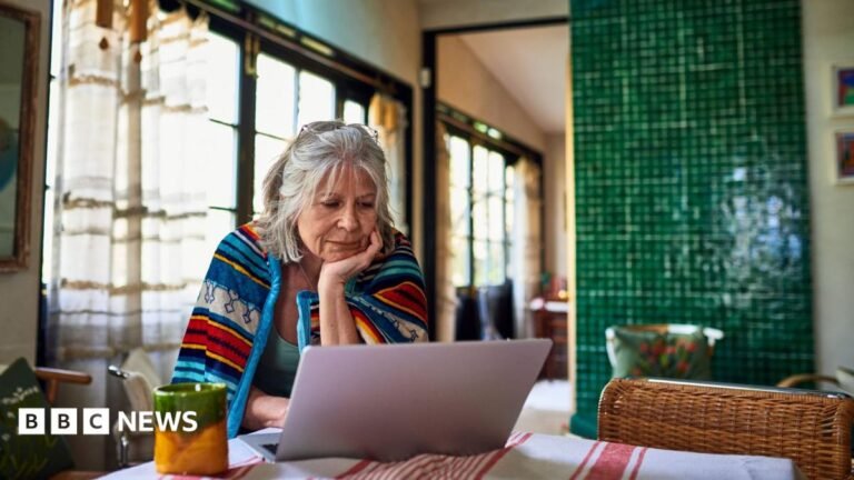 Triple lock move is significant, but it’s a gamble A pensioner looks at her finances on her laptop at her dining room table. She is wearing a colourful throwover.
