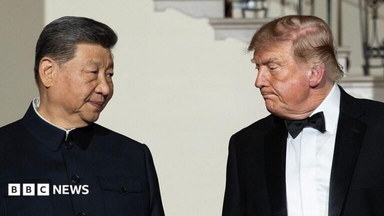 Xi Jinping and Donald Trump stand facing each other during a formal event, with Xi wearing a dark high-collared jacket and Trump wearing a black tuxedo with a bow tie.