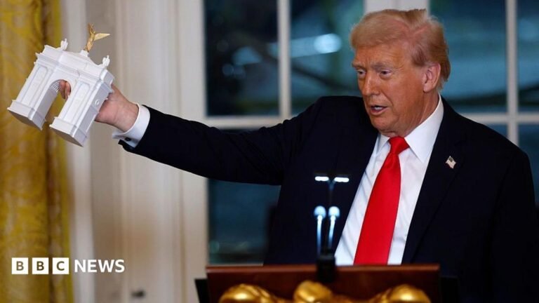 Trump says his triumphal arch will become a military ammunition complex Trump holding up a tiny model of a triumphal arch in the White House