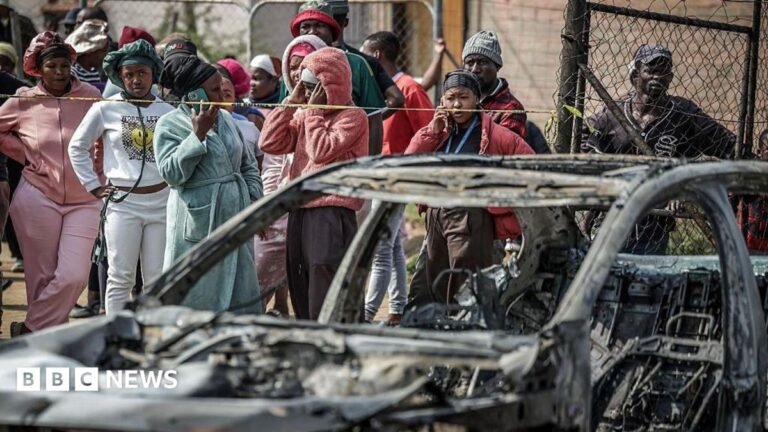 Two mass shootings in South Africa leave 27 dead A crowd of people look on close to a burned out car