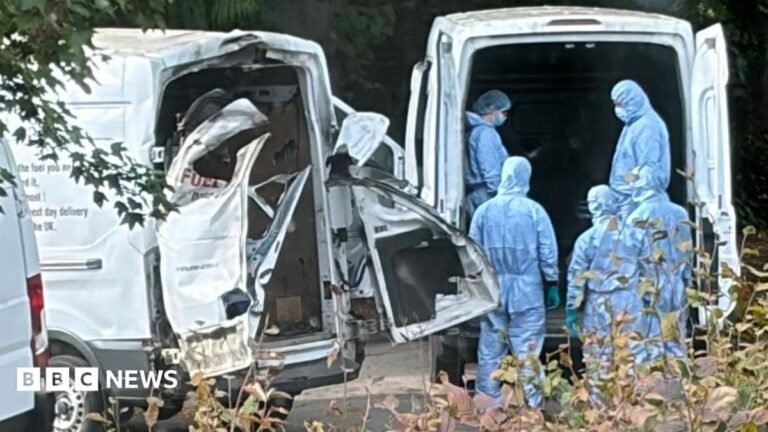 UK believes Iran involved in RAF Fairford incident, Burnham says people in blue hazmat suits stand behind a white van next to another white van with the back doors blown off
