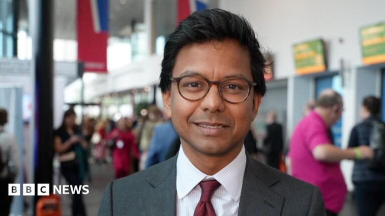 UK needs plan in case of ‘unprecedented’ AI job losses, says minister Kanishka Narayan, wearning dark rimmed glasses and a suit and tie, poses for the camera at a party conference