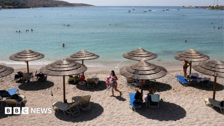 Vouliagmeni beach: Man, 82, dies after beach fight with 76-year-old over sunlounger in Greece The beach with the sea in the background. There are sun beds and straw shades