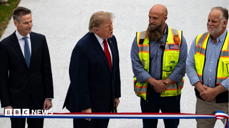 Trump, dressed in a suit, stands next two two men with high-viz jackets to his left and a man in a dark suit to his right at a ribbon-cutting ceremony for a new helipad on the South Lawn of the White House in Washington, 21 September 2026