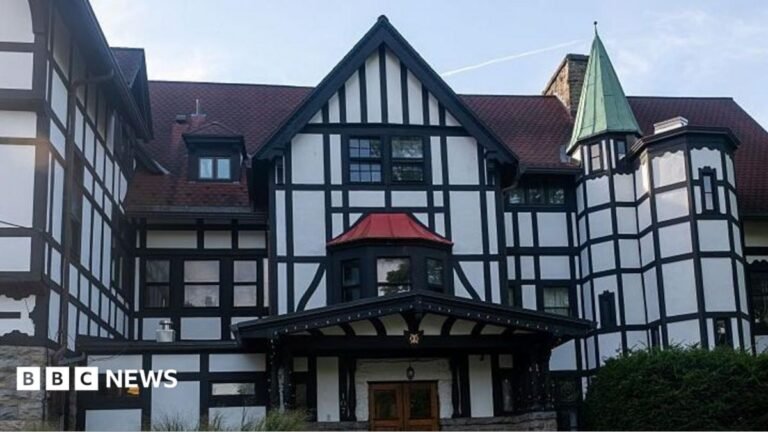 A large, black and white white multi-storey house with a red tiled roof.