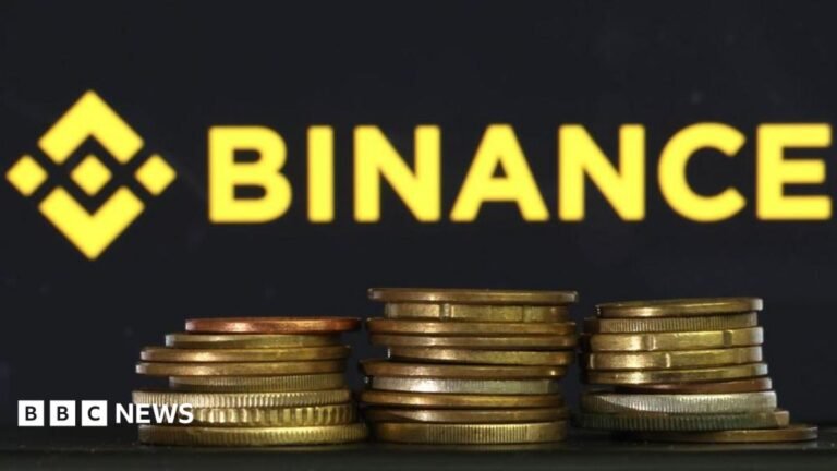 In this photo illustration, the Binance logo is displayed on a screen behind a stack of gold coins.