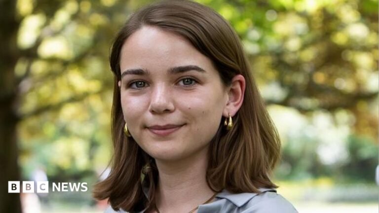 Dread presenting at work? Read these tips before your next meeting A woman with short brown hair in a bob smiling, she is wearing gold hoop earrings and a blue blouse. The background is blurred but features a large green tree.