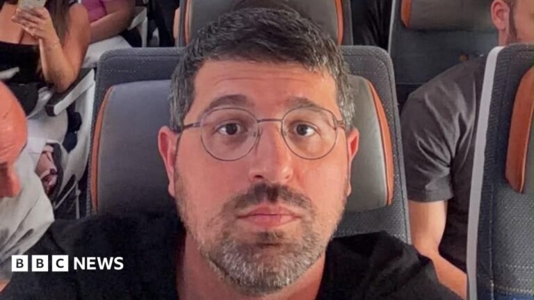 Flydubai passenger describes hugging his children as plane nosedived during attack A selfie of Adam Polo sitting on a busy aeroplane with a grey and orange seat cushion. He has short dark hair and a beard and is wearing glasses and a black t-shirt