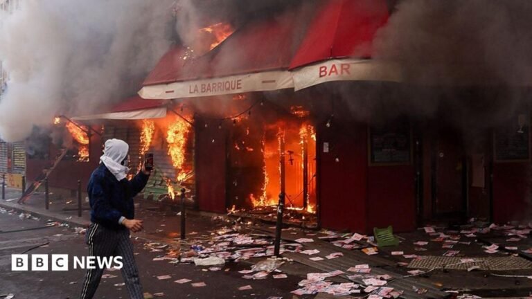 A man films as smoke rises from the bar 'La Barrique' on the sidelines of a demonstration against the "high cost of living", in Paris.
