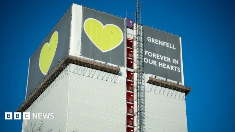 Grenfell tenants firm could face corporate manslaughter charge Grenfell Tower covered in protective white sheeting during dismantling work, with scaffolding and a green crane above a memorial wall decorated with hearts, photographs and tributes.