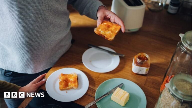 Healey vows cheaper marmalade and gherkins in pre-Budget package A man is visible from the chest down standing at a table eating marmalade on toast with a woman's hand visible in the shot.