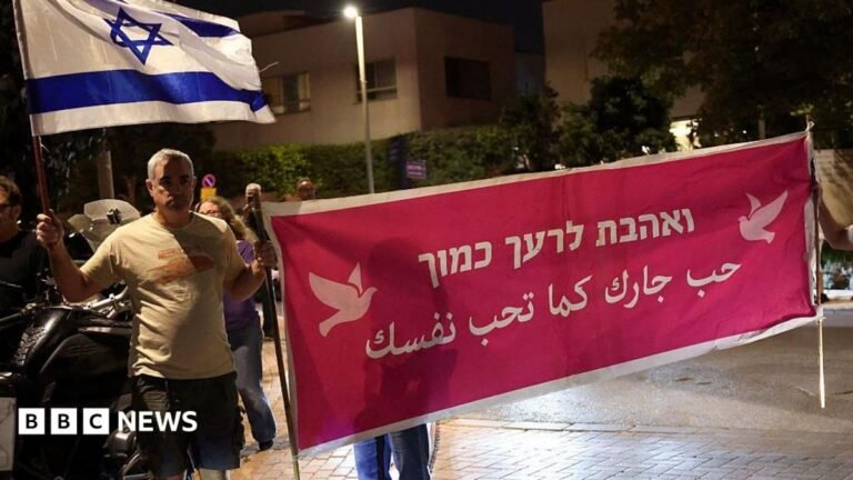 People demonstrate holding a banner that says "Love your neighbour" in Arabic and Hebrew
