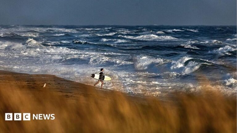 Medical plane with 6 on board missing off Massachusetts coast A man carries a surfboard on a beach