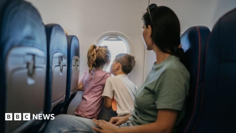 Move to stop charges for parents to sit by children on flights A dark-haired woman watches on as two children look through an aeroplane window.