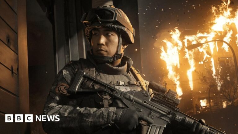 An in-game screenshot showing a male Korean soldier holding a gun with a building on fire behind him.