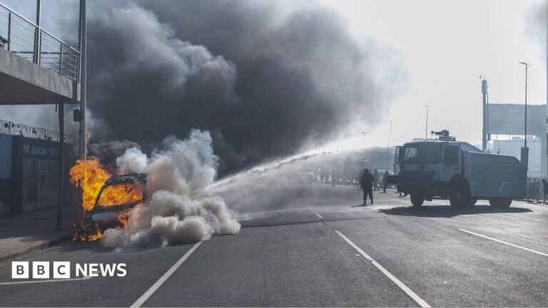South African anti-migrant protests: Cars torched and shops looted in Durban and Soweto A vehicle burns on the side of a road as thick black smoke fills the air, while a police water-cannon truck sprays water towards the scene