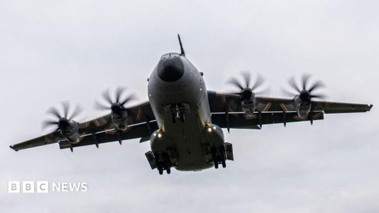 UK to draft in military aircraft to fight wildfires, Burnham says Large waves crashing over a black and white striped lighthouse at the end of a pier.